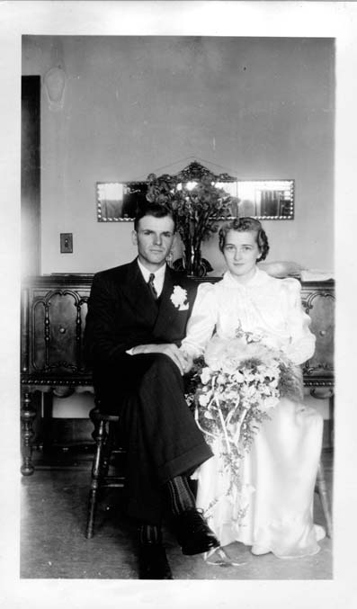A young man and woman sit in their wedding dress and suit. The woman is holding a bouquet of flowers, and the man has a flower boutonniere.