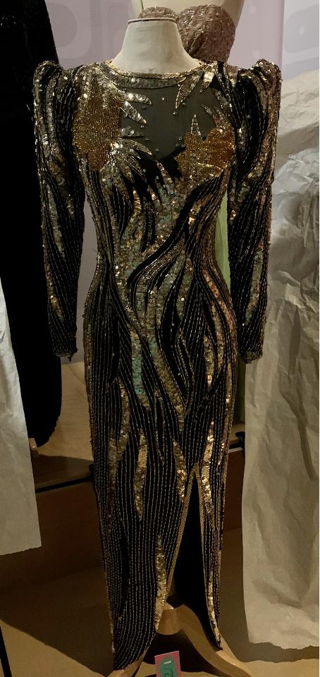 A full length dress with long sleeves and large shoulders. The dress is black with gold sequins throughout.